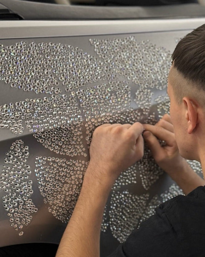 Person applying crystal vinyl wrap to a car in a garage setting.