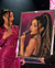A large framed portrait artwork made of sparkling rhinestones showing a woman with a high ponytail holding a microphone, held by two people on a stage. One person wears a bright pink sequined dress, and the background includes a pink patterned screen.